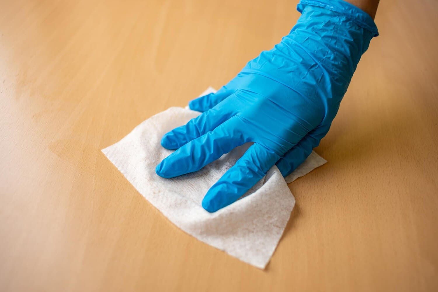 Gloved hand wiping a wooden surface with a cleaning cloth
