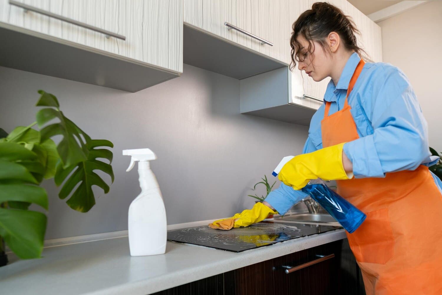Cleaner in rubber gloves spraying and wiping a kitchen worktop
