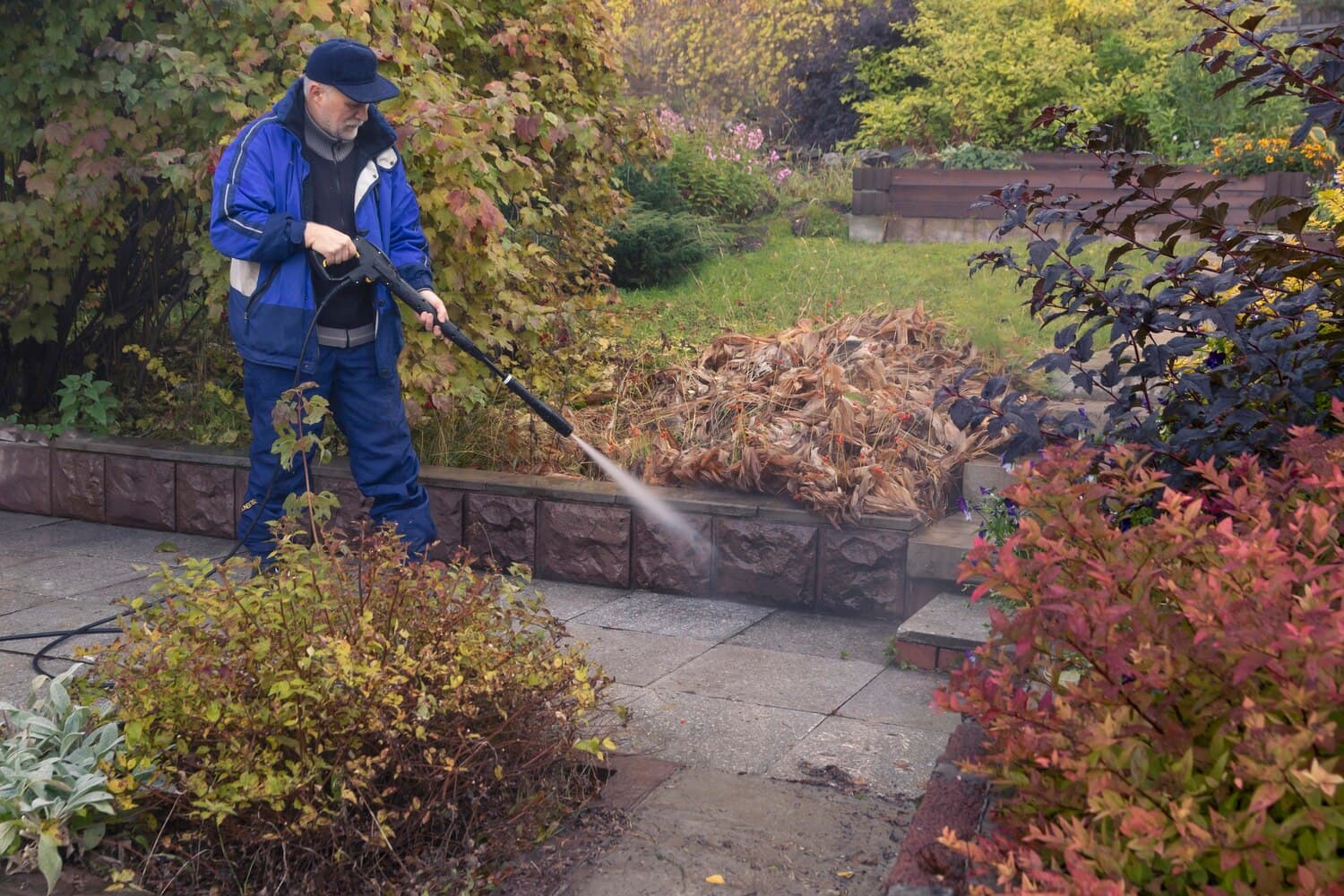 Pressure-washing a garden path beside autumn planting