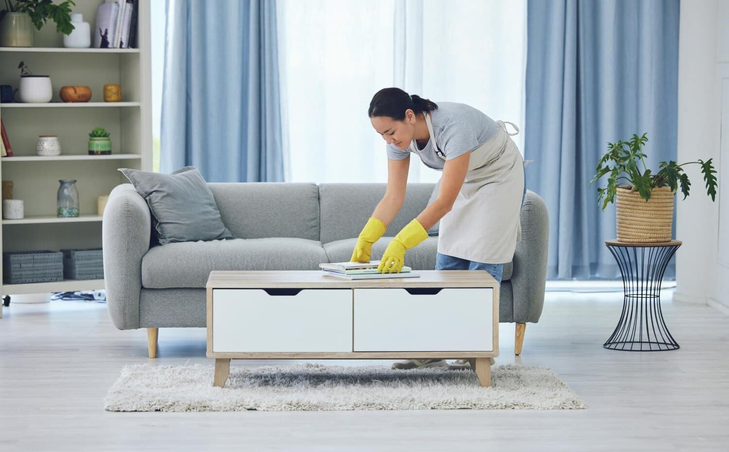 Cleaner in yellow gloves tidying a coffee table in a bright living room