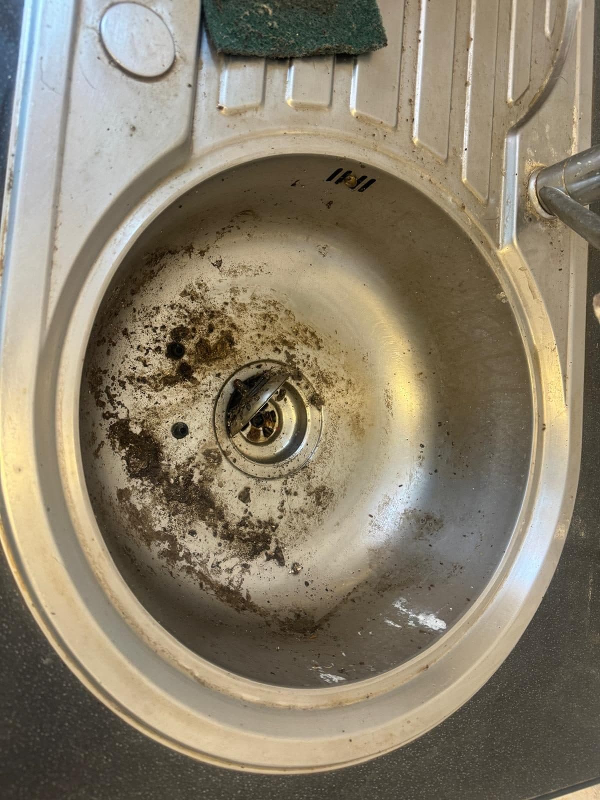 Stainless steel sink covered in dark residue before cleaning